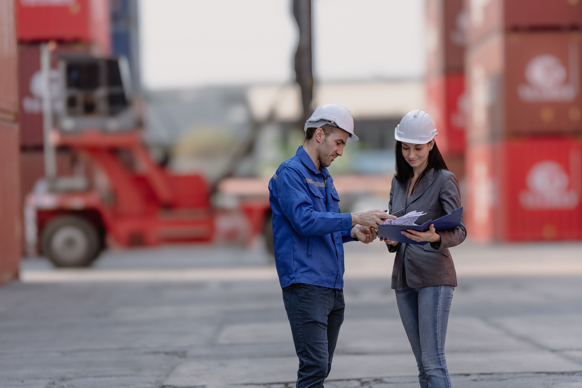 Foreman worker wear safety hardhat standing inspecting container cargo at warehouse storage terminal. Industrial engineer woman working at import export distribution port.